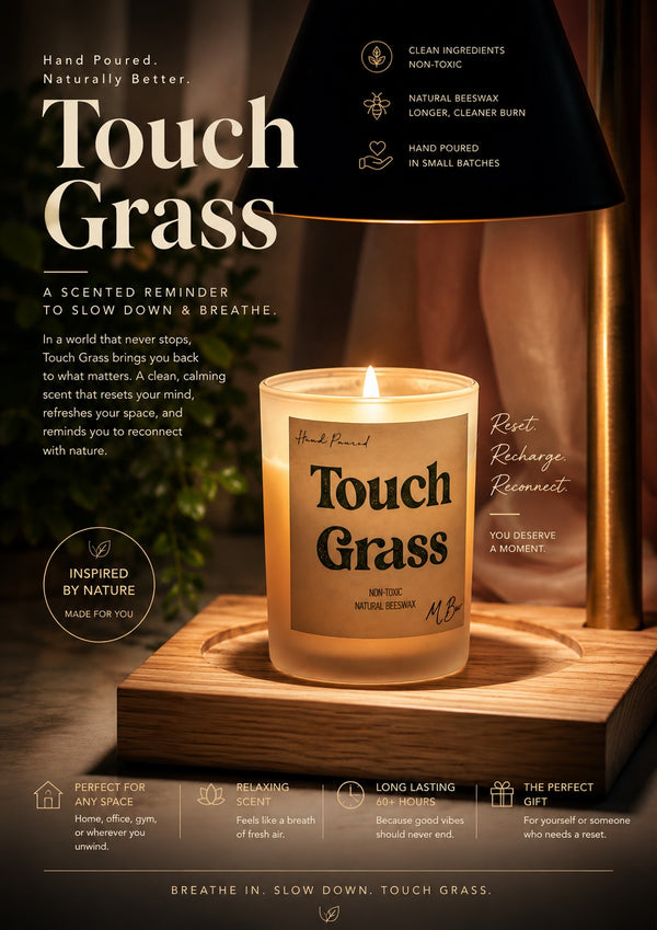 A lit scented candle labeled 'Touch Grass' by MBurr, displayed on a wooden surface with a dark lamp and warm ambient lighting in the background.