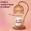 A lit amber glass bell-shaped lamp with a curved metallic arm and wooden base sits above a candle jar labeled 'Do Not Disturb' on a soft pink background with decorative text.