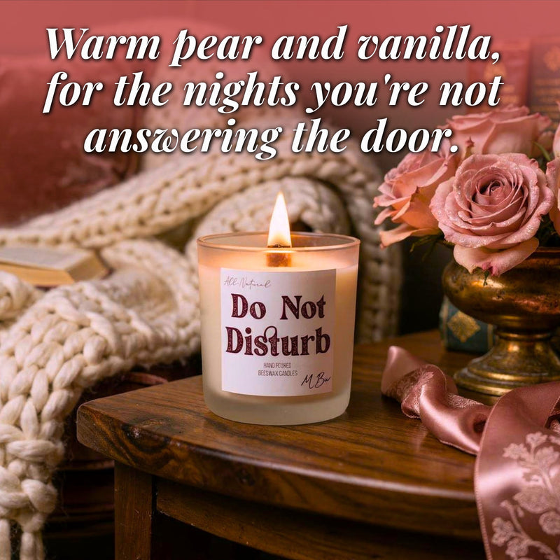 A lit candle in a frosted glass jar sits on a wooden table beside pink roses in a gold urn, with a chunky knit blanket and overlaid text reading, 'Warm pear and vanilla, for the nights you're not answering the door.'.