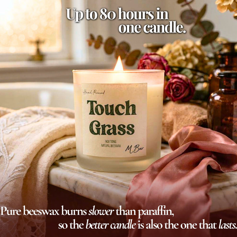 Lit Touch Grass beeswax candle on marble bath ledge with roses