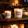 Two lit Wine Down beeswax candles by fireplace with wine and figs